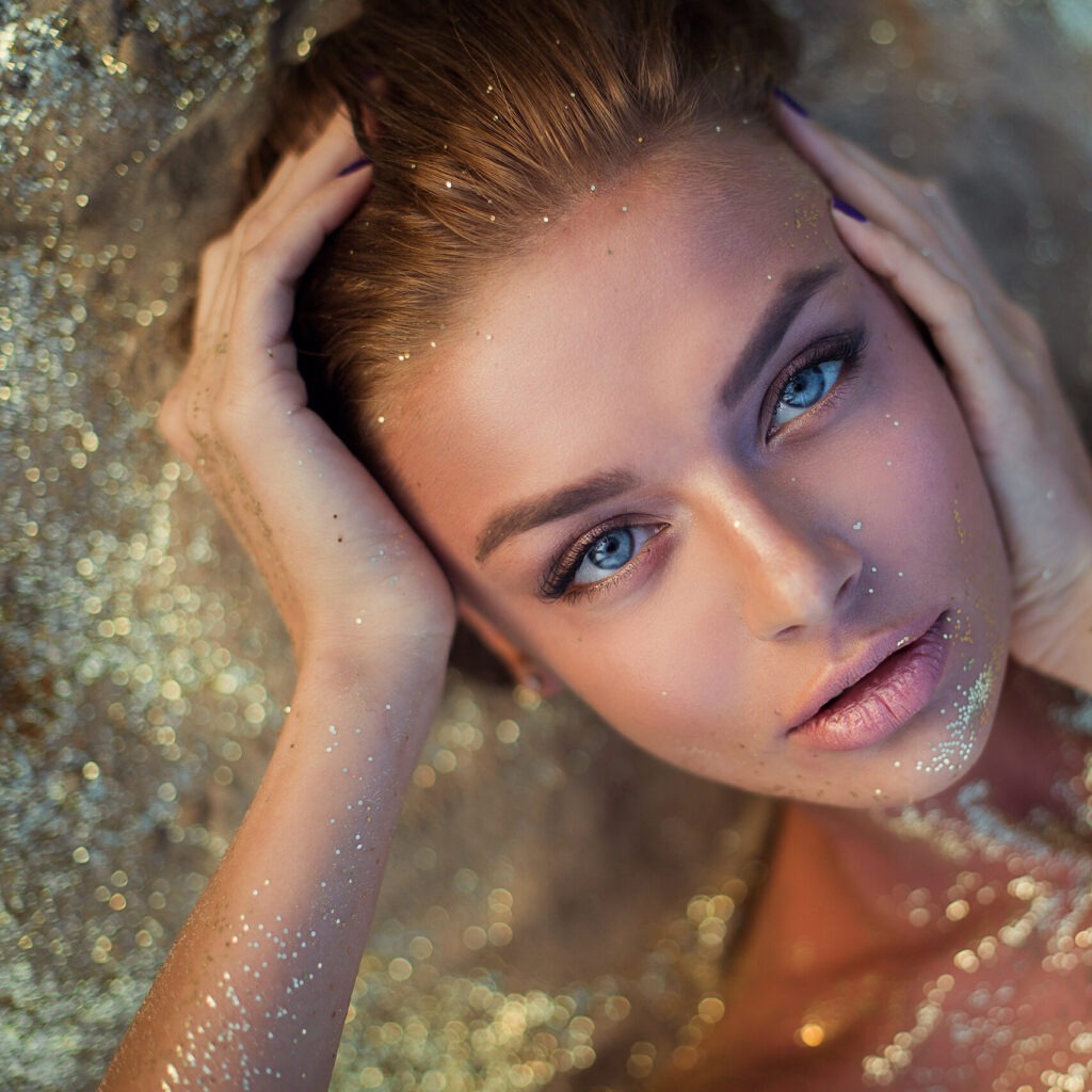 very beautiful woman with incredible blue eyes lies on the golden glitter on her face and body