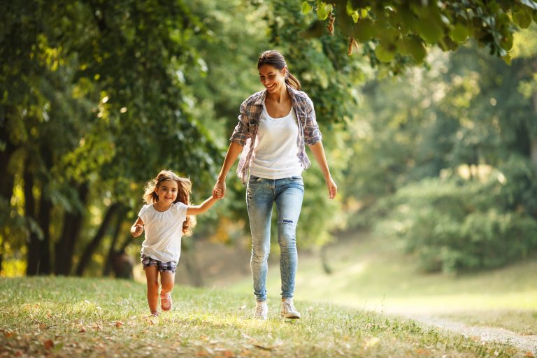 Happy mom and daughter holding hands and walking in a beautiful forest | Mommy Makeover