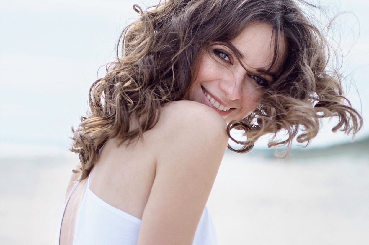 Happy woman on the beach. Portrait of the beautiful girl close-up, the wind fluttering hair. Spring portrait on the beach. Young pretty girl. Young smiling woman outdoors portrait.