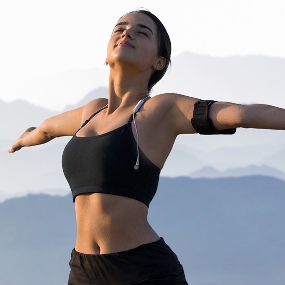 A thin athletic girl takes a break between classes on the background of mountains in the early morning, enjoys silence and freedom.