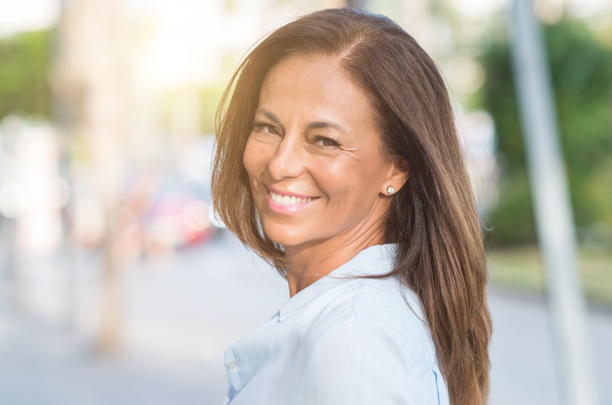 Beautiful middle age hispanic woman at the city street on a sunny day with a happy face standing and smiling with a confident smile showing teeth