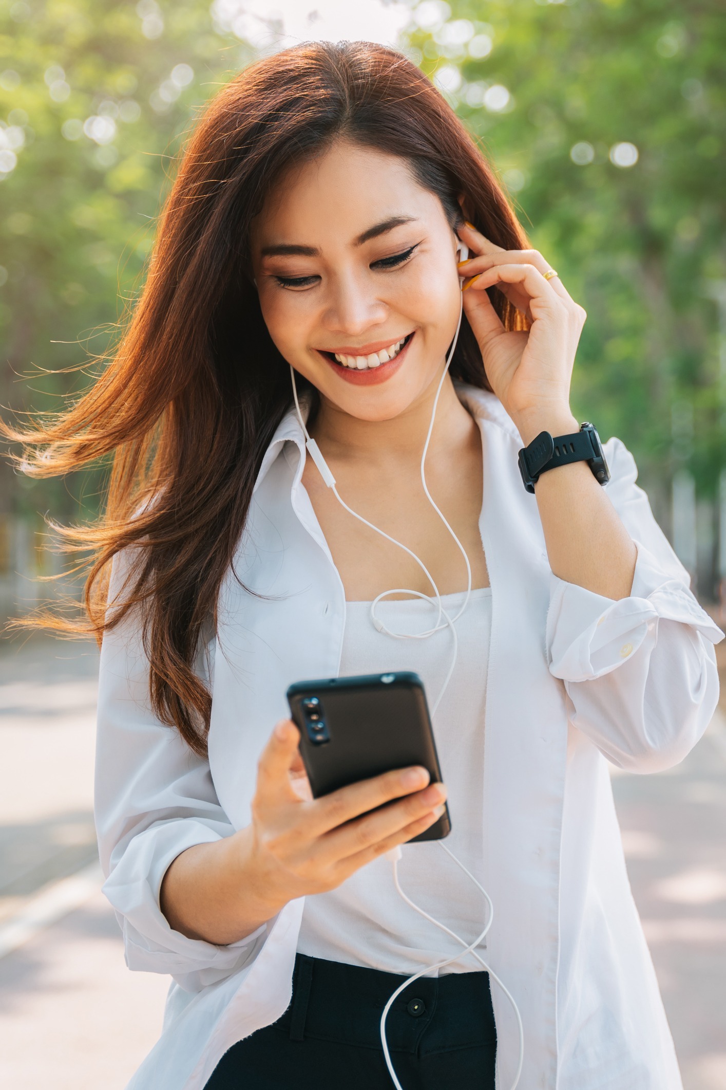 Asian woman using the small talk headphones to make a happy phone call in the park.