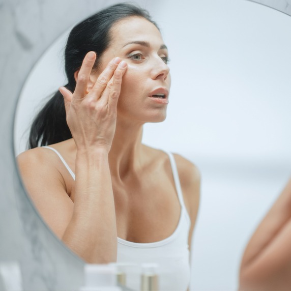 Portrait of Beautiful Caucasian Woman Gently Applying Face Cream Mask with Sensual Gestures, Looking in Bathroom Mirror. Middle Aged Female Makes Skin Soft with Natural Cosmetics Skincare Product