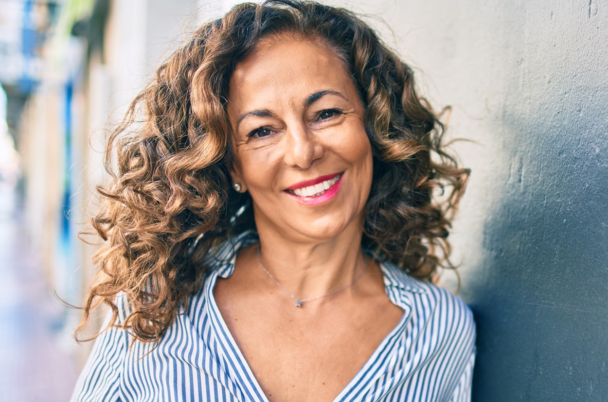 Middle age hispanic woman smiling happy leaning on the wall at the city.