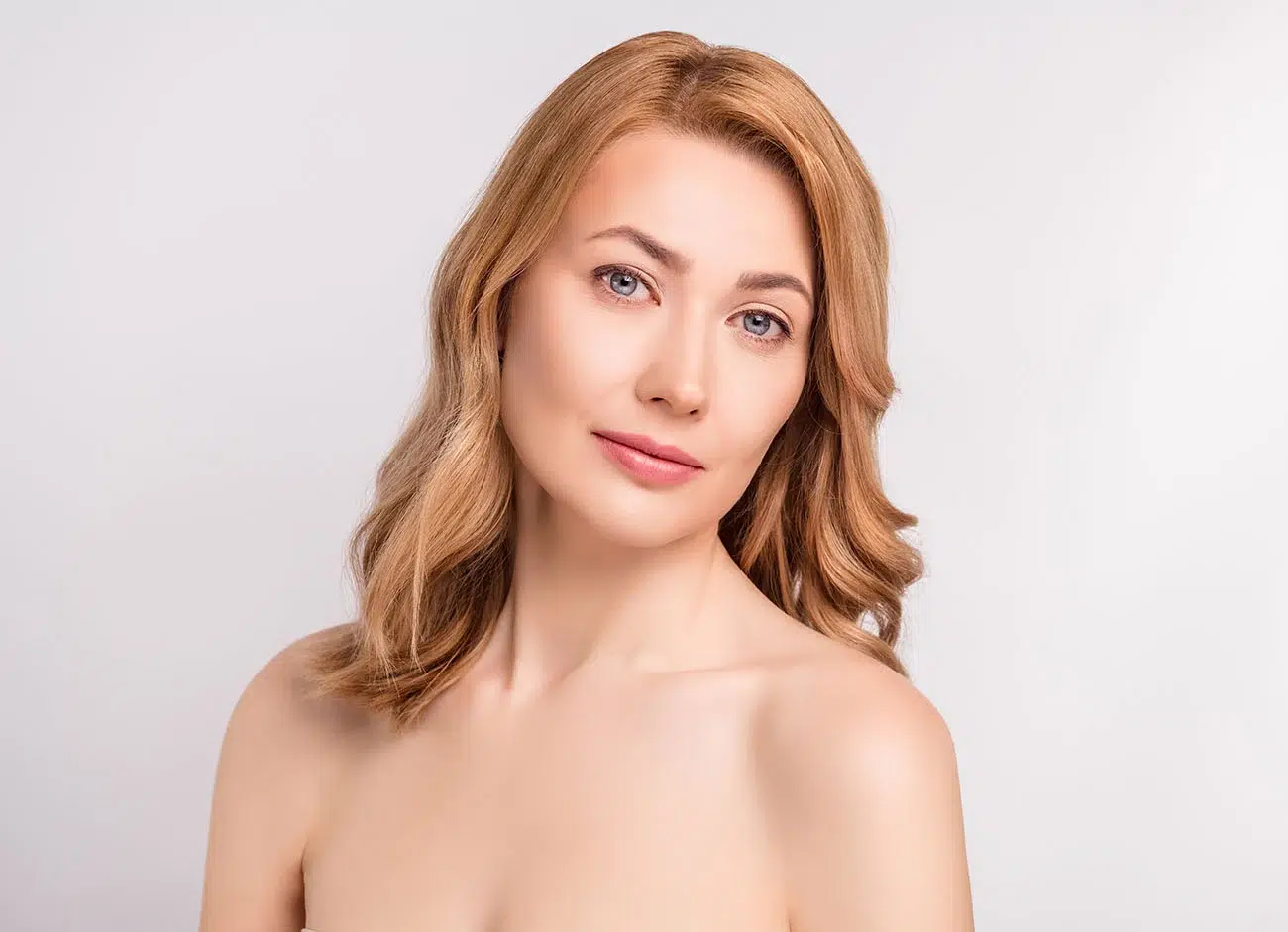 Portrait of a woman with wavy auburn hair and blue eyes against a neutral white background, highlighting smooth skin.